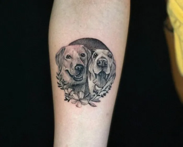 Pet tattoos featuring two dogs surrounded by flowers on an arm, symbolizing the bond with pets.