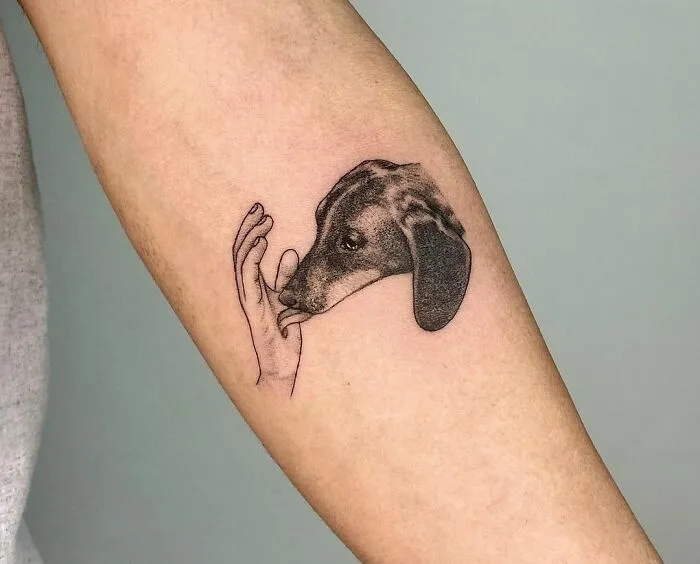 Pet tattoo of a dog's head with a hand on a person's forearm.