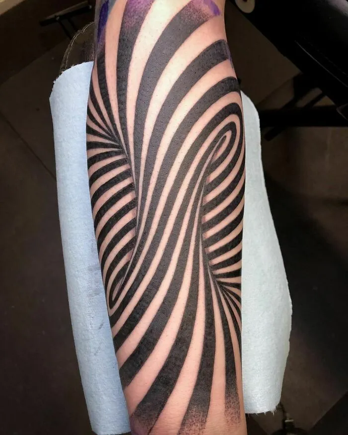 Optical illusion tattoo with black spiral design on an arm, creating a mind-bending effect.