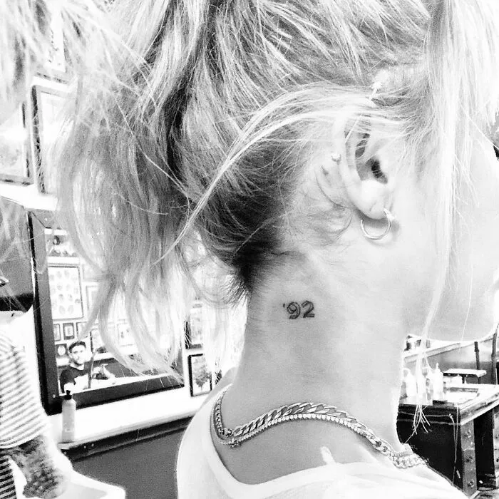 Celebrity tattoo of '92 on the back of a woman's neck in a tattoo studio.
