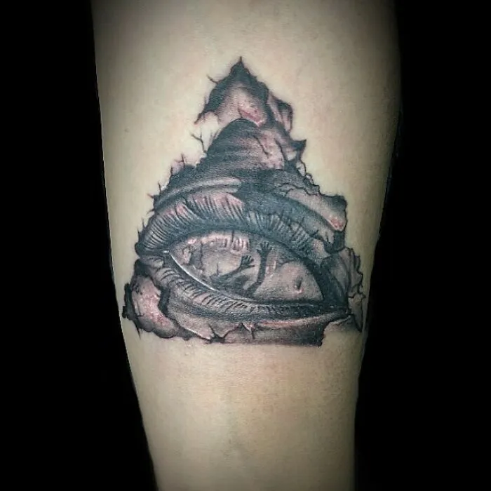 Optical illusion tattoo design featuring a realistic eye within a cracked triangular shape.