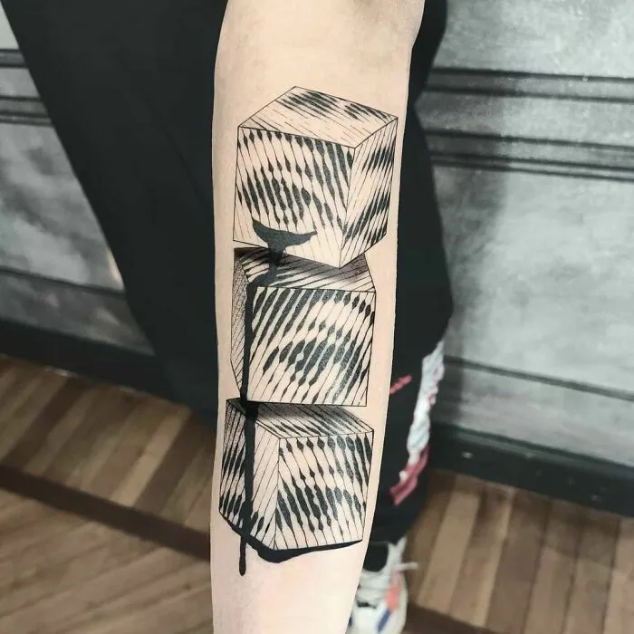 Optical illusion tattoo design of three stacked cubes with striped patterns on a forearm.