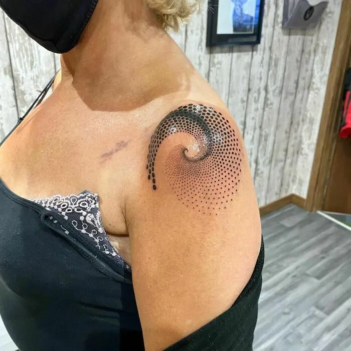 Optical illusion tattoo design with spiral dots on a woman's shoulder.