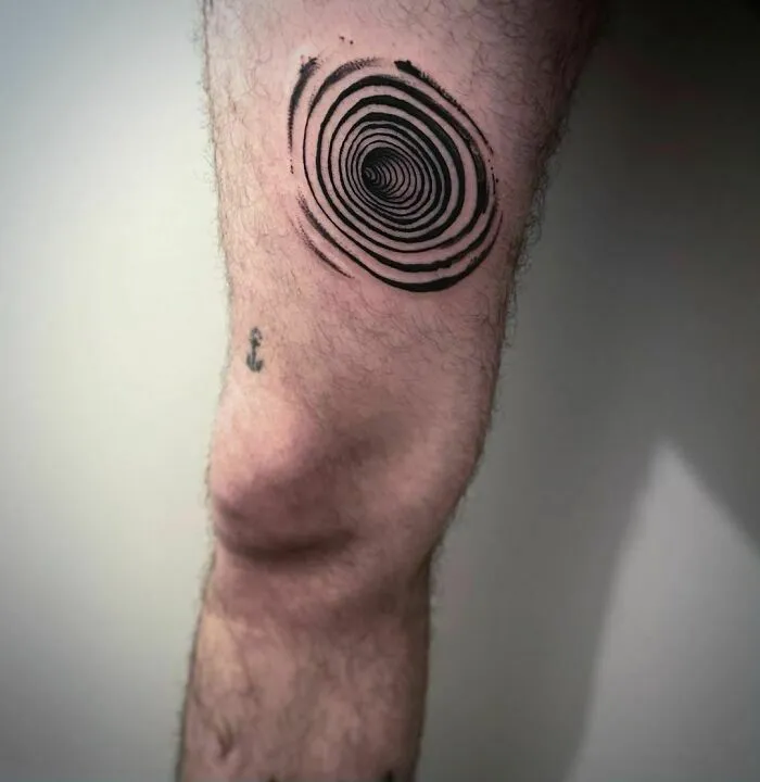 Optical illusion tattoo on leg, featuring a spiral design above the knee.