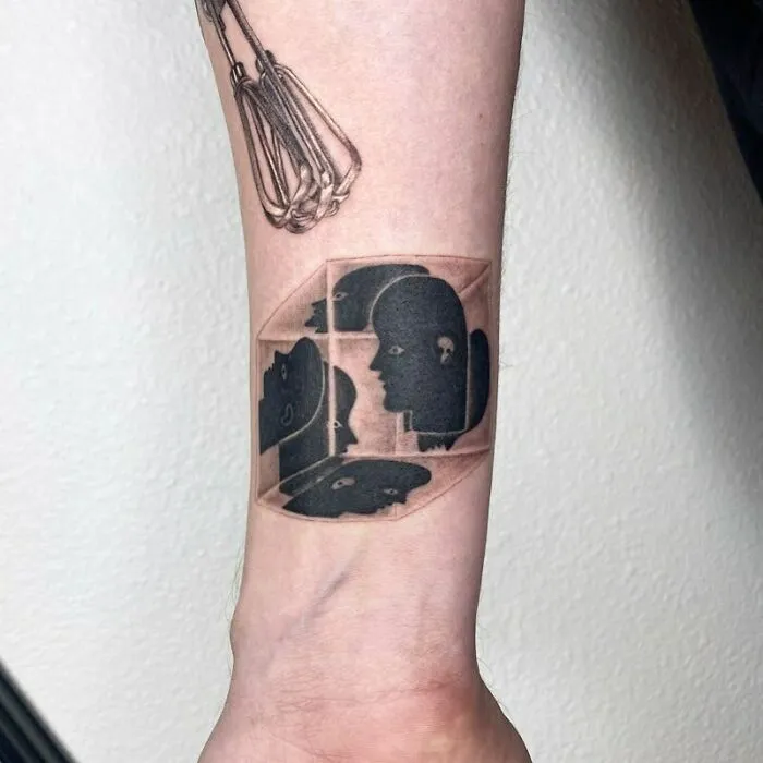 Optical illusion tattoo featuring faces in a 3D cube design on a forearm.