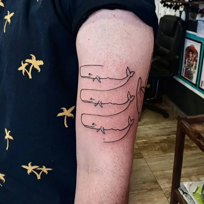 Arm with optical illusion tattoo of overlapping whales in a line.