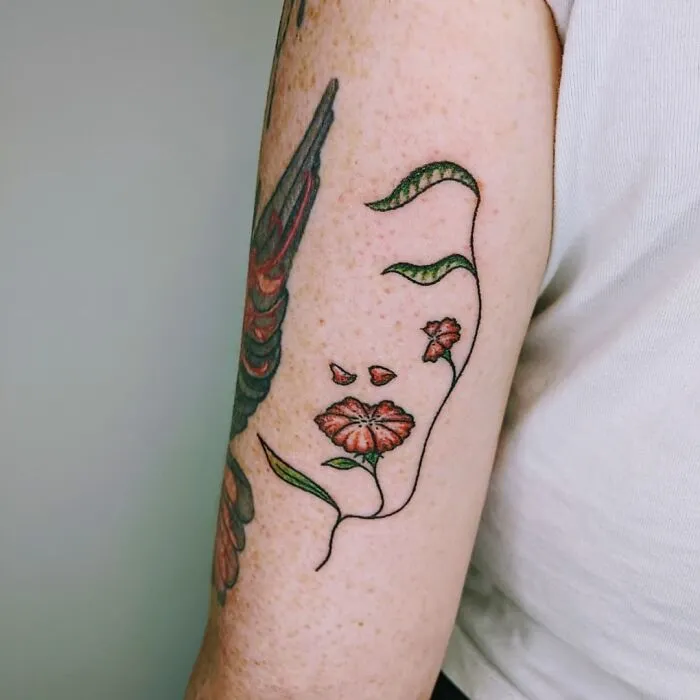 Optical illusion tattoo featuring flowers forming an abstract face on an arm.