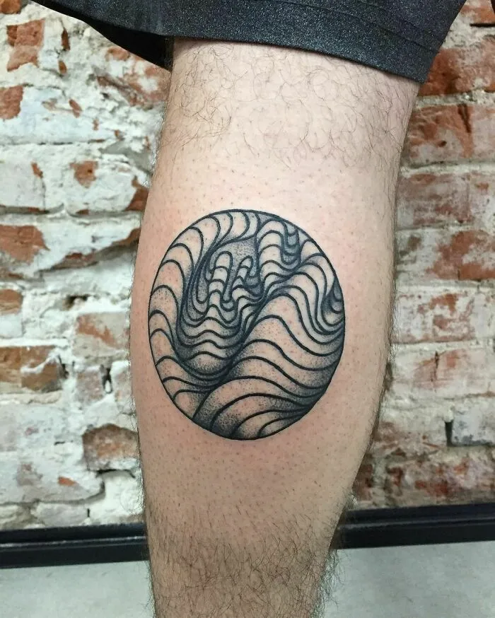 Optical illusion tattoo on leg with swirling lines creating a 3D effect, set against a brick wall background.