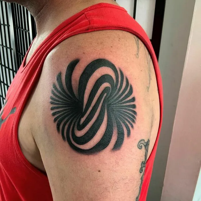 Optical illusion tattoo design with swirling black patterns on a person's upper arm wearing a red tank top.