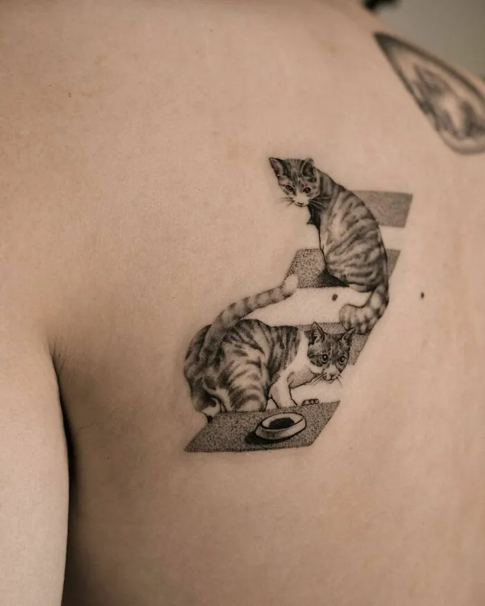 Optical illusion tattoo of two cats on a person's upper back, creating a dynamic, mind-bending design.