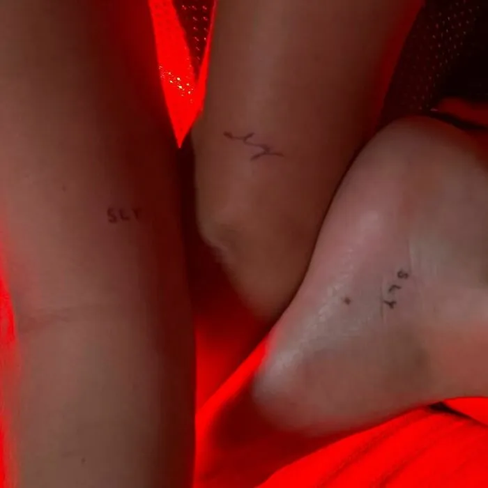 Three small celebrity tattoos on skin with red lighting, featuring simple text designs.