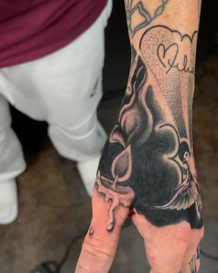 Intricate optical illusion tattoo on hand with candle, rose, and bird design.