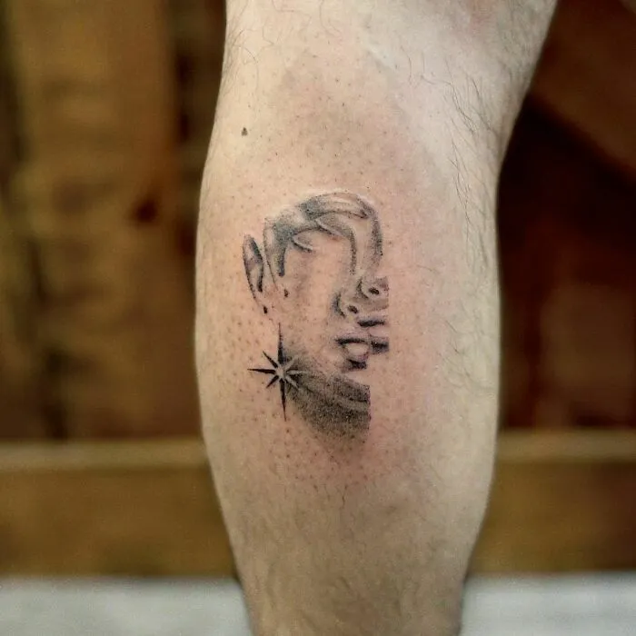Optical illusion tattoo on calf, featuring face and star design, creating a mind-bending effect.