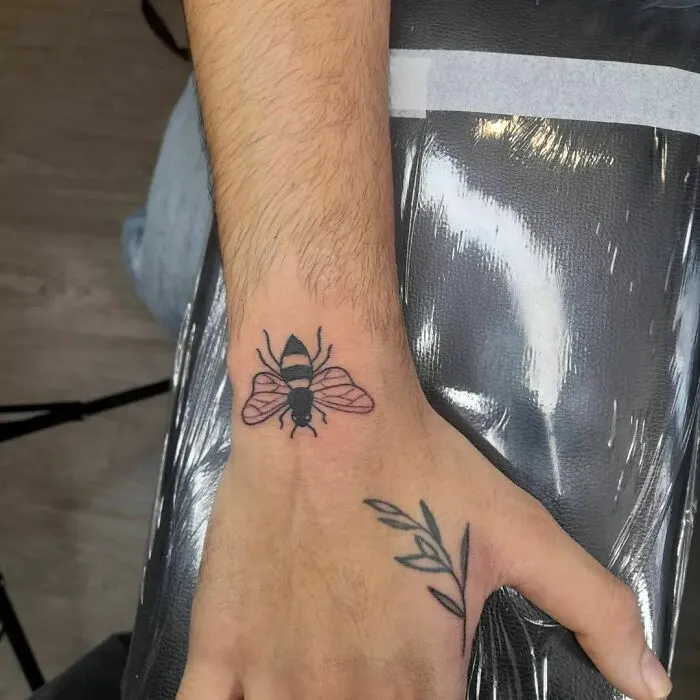 Minimalist bee tattoo on a person's wrist, showcasing aesthetically pleasing design and simplicity.