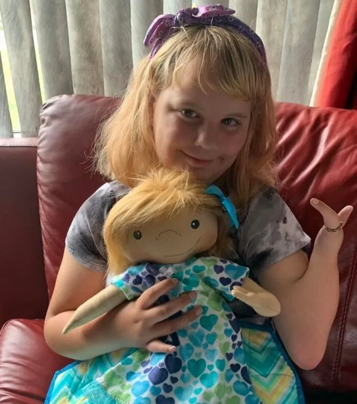 A girl with a purple headband smiles while holding a custom doll that represents herself.