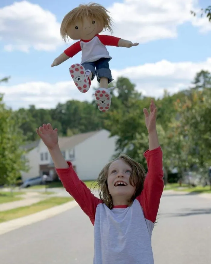 A joyful child throws a custom doll representation of himself high into the sunny sky.