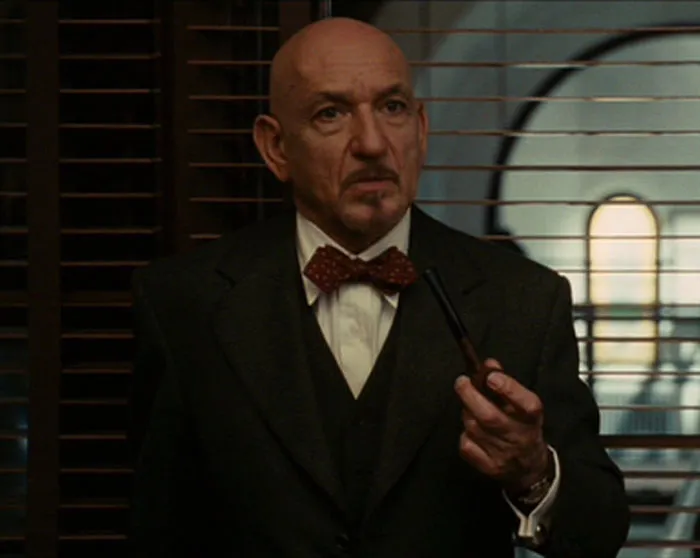 Ben Kingsley in a grey jacket holding a pipe in a scene from Shutter Island, illustrating famous people married multiple times.