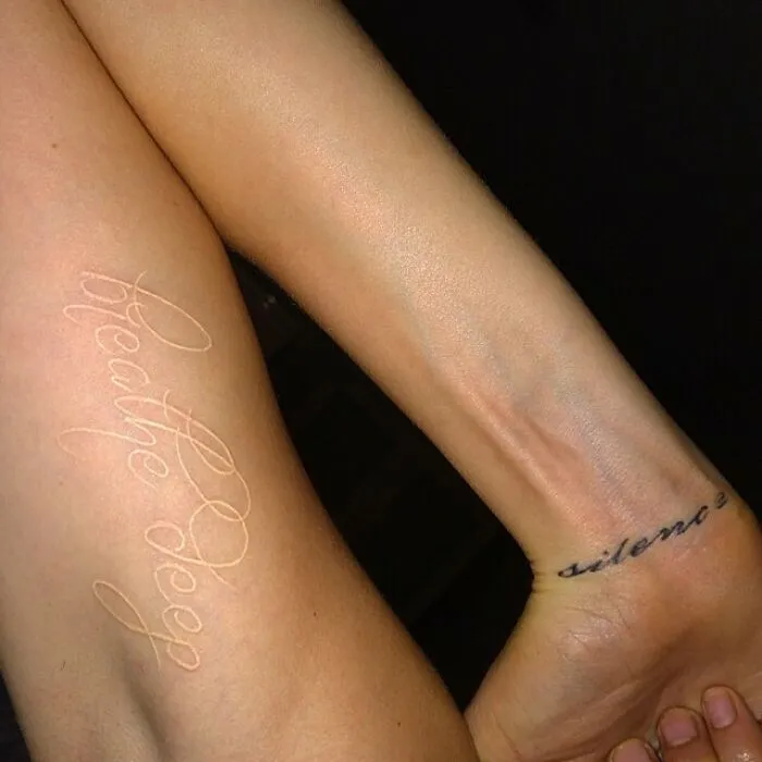 Celebrity tattoos on arms with words "breathe deep" and "silence" in delicate script.