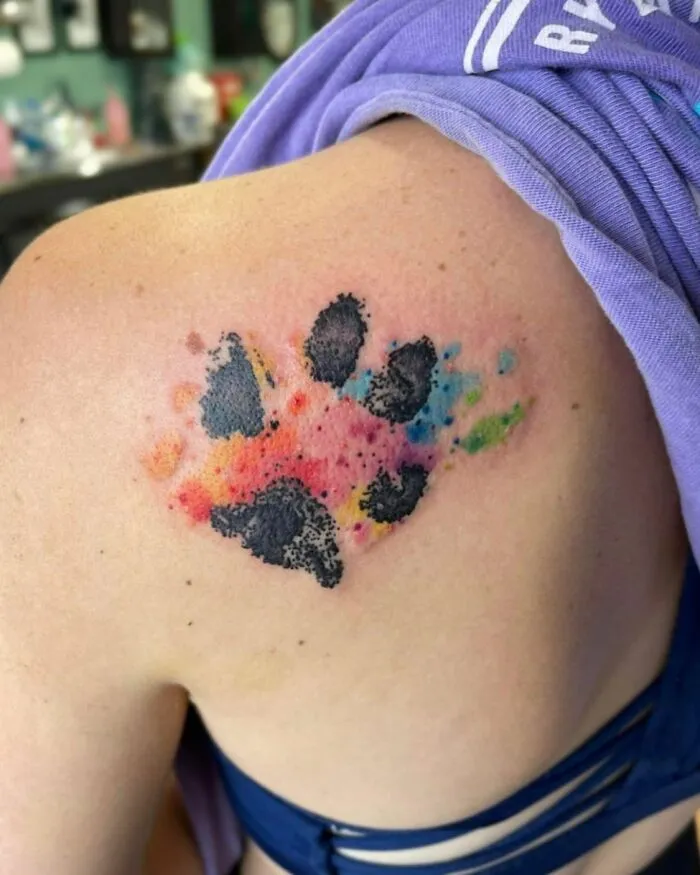 Watercolor tattoo featuring a vibrant paw print design on a person's shoulder.