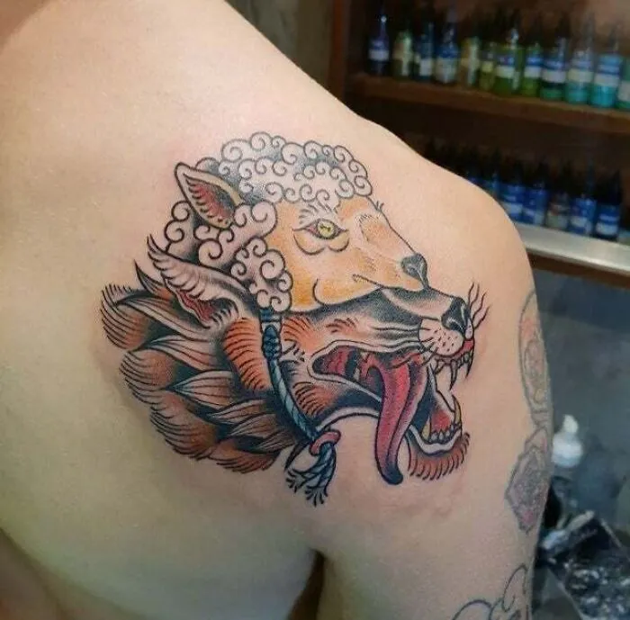 Psychedelic art tattoo of a wolf and a sheep on a person's shoulder.