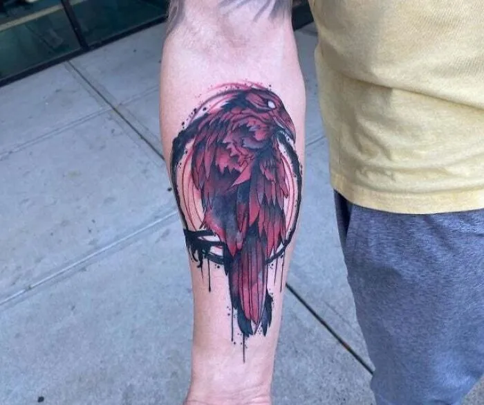 Forearm tattoo of a red and black crow, showcasing psychedelic art elements.