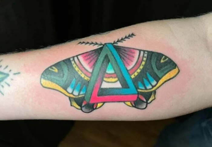 Psychedelic art tattoo of a colorful butterfly with a geometric triangle design on an arm.