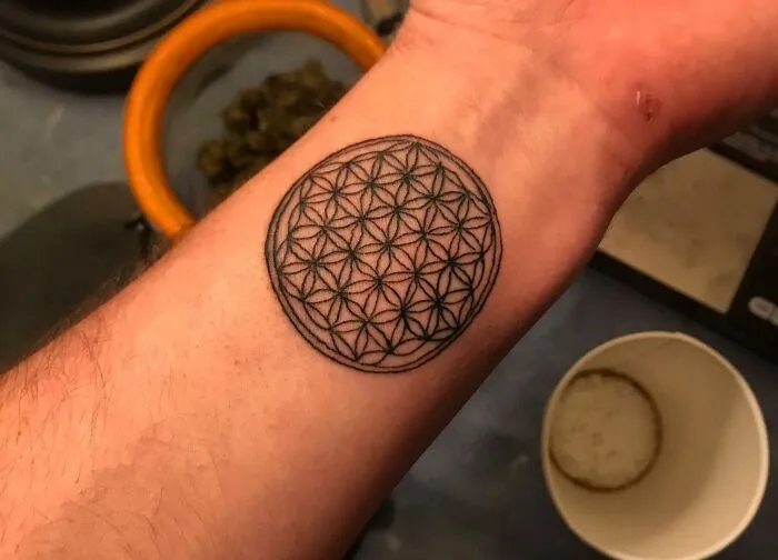 Psychedelic art tattoo on forearm featuring geometric circle design.