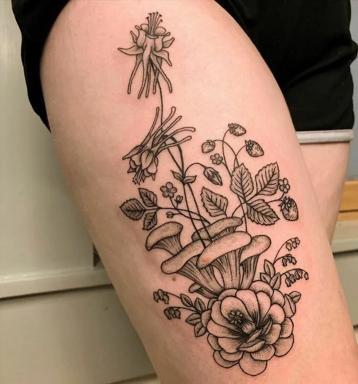 Nature tattoo featuring flowers and mushrooms intricately designed on the upper thigh, celebrating the wonders of Mother Earth.