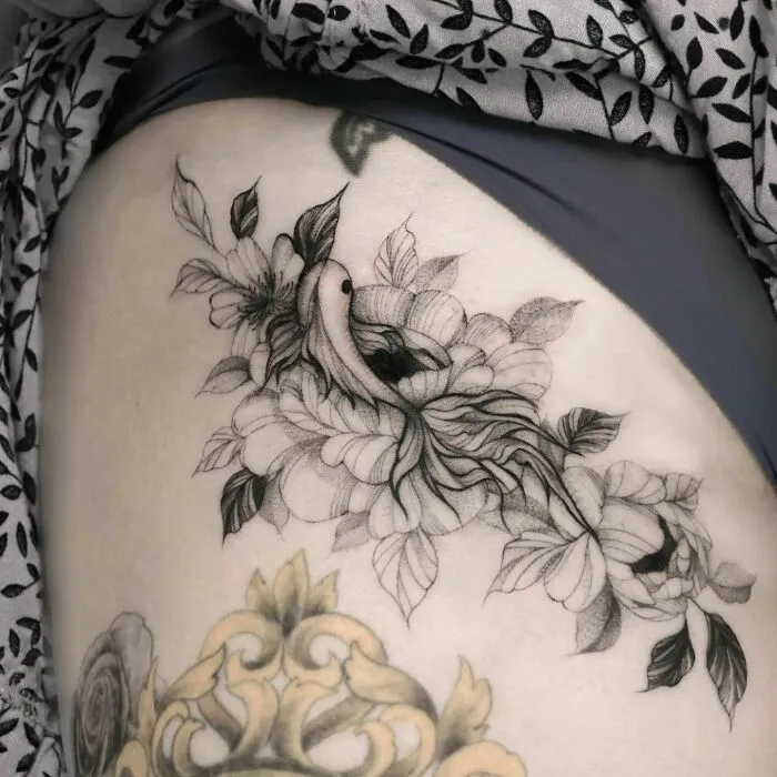 Nature tattoo featuring a bird nestled among detailed flowers on a person's skin.