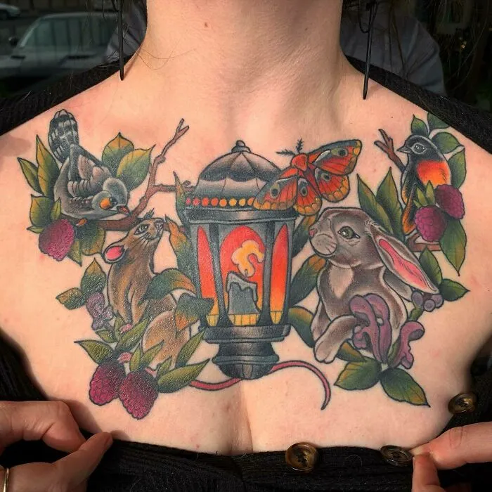 Nature tattoo featuring animals, lantern, and foliage on a person's chest, celebrating Earth’s wonders.