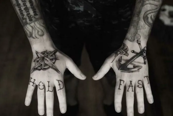 Hands with "HOLD FAST" word tattoos and nautical designs.