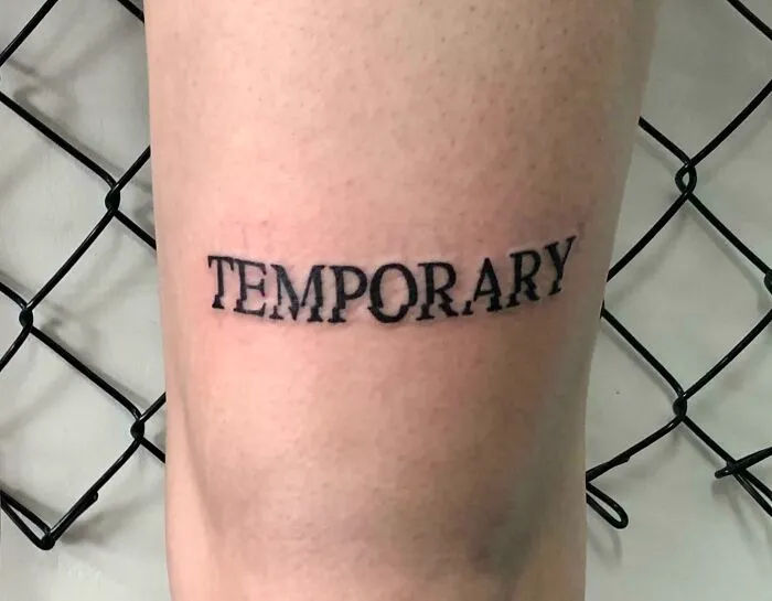 Black "Temporary" tattoo on inner arm, showcasing creative word tattoos for inspiration.