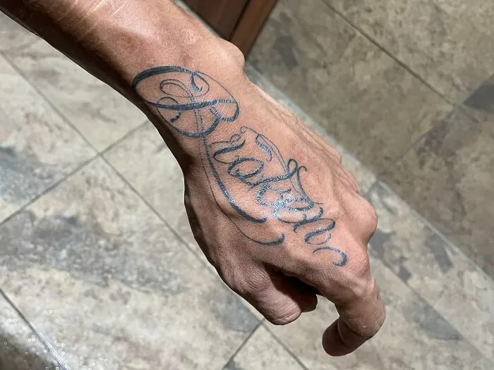 Hand with elegant word tattoo reading "Broken" in cursive script, highlighting creative word tattoos for inspiration.