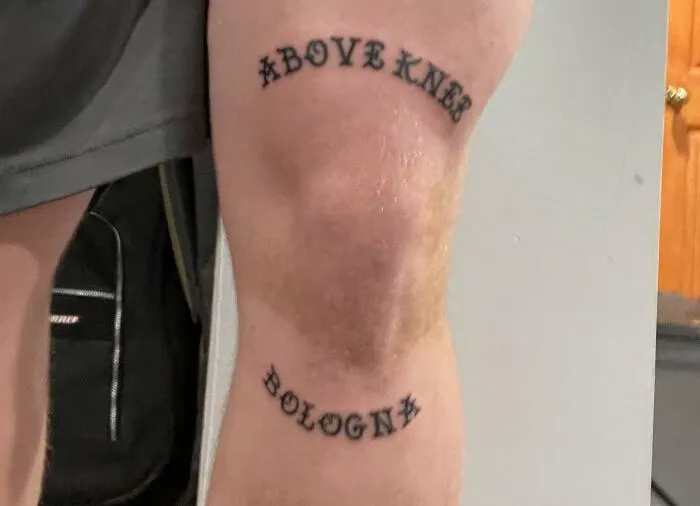 Tattoo on a knee reading "Above Knee Bologna" in bold, black letters.