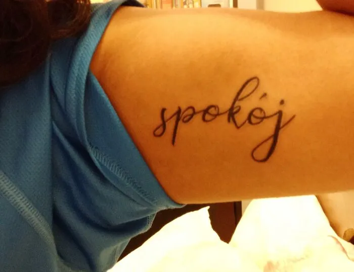 Tattoo of the word "spokój" in cursive font on a person's upper arm.
