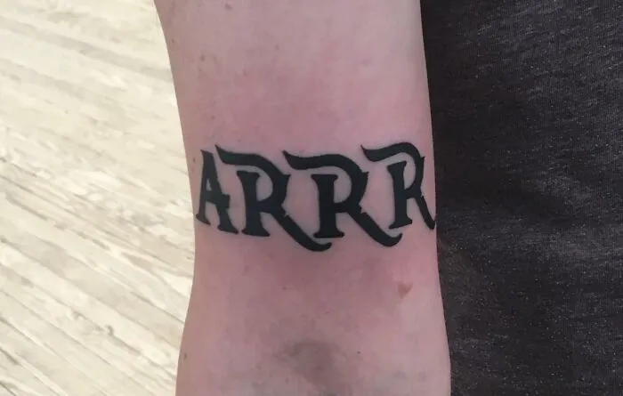 Arm tattoo with the word "ARRR" in bold black letters on light skin.
