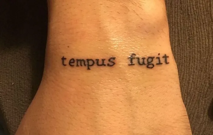 Tattoo of the phrase "tempus fugit" on a person's wrist.