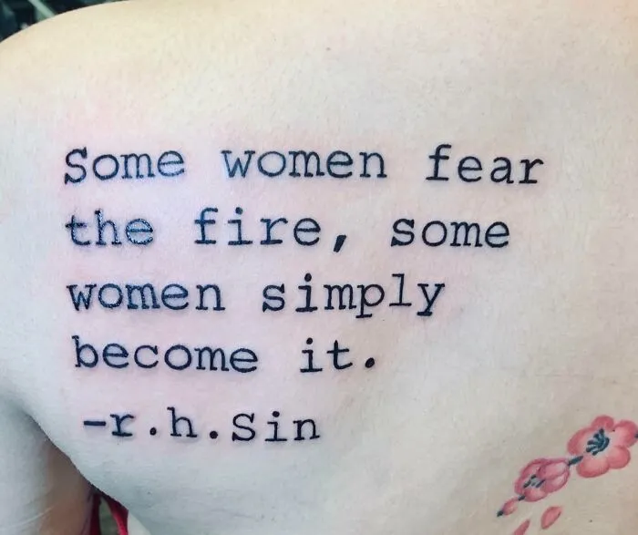 Tattoo with the quote "Some women fear the fire, some women simply become it" by r.h. Sin, with a floral design below.