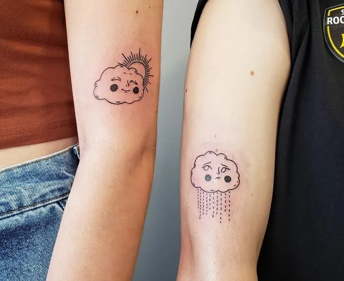 Two arms with matching cloud tattoos symbolizing friendship; one sunny, one rainy.