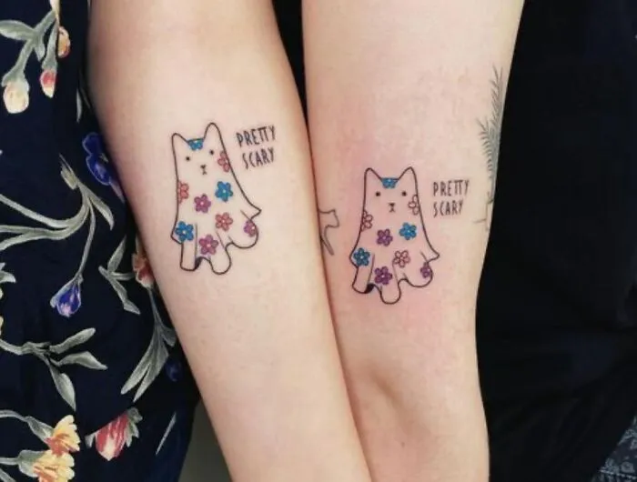 Matching best friend tattoos with floral ghost designs and "Pretty Scary" text on forearms.