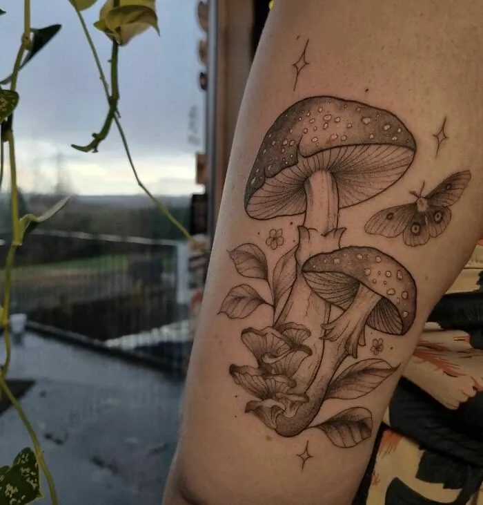 Nature tattoo of mushrooms and a moth on an arm, celebrating Earth’s wonders.