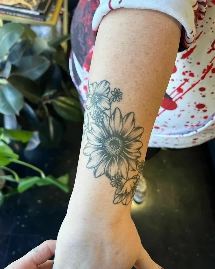Floral nature tattoo on forearm featuring detailed daisy and leaves design.