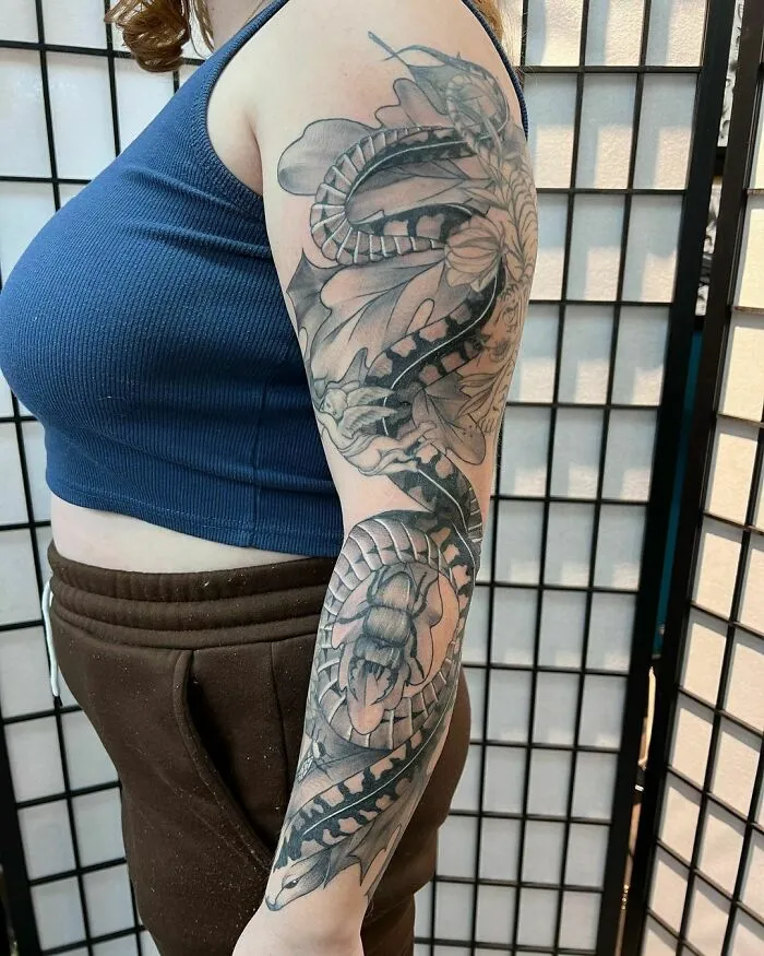 Detailed snake and floral nature tattoo on a woman's right arm in a blue top.