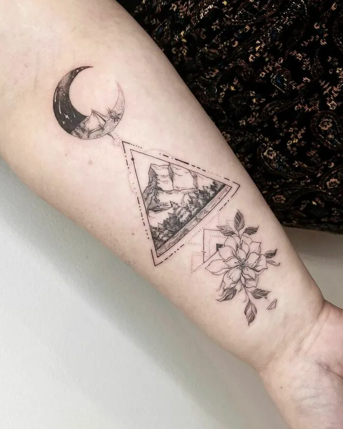 Nature tattoo featuring a crescent moon, mountain landscape, and flower on forearm.