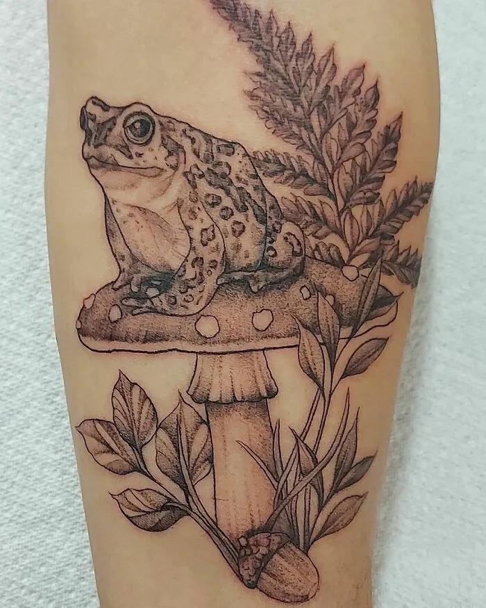 Nature tattoo featuring a detailed frog sitting on a mushroom with leaves and ferns.
