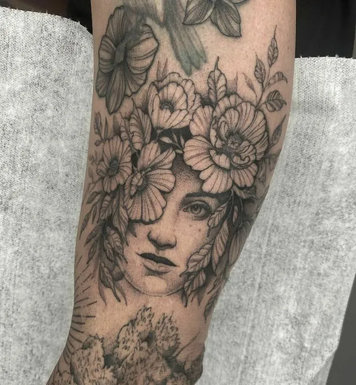 Nature tattoo featuring a woman's face surrounded by detailed flowers and leaves on forearm.