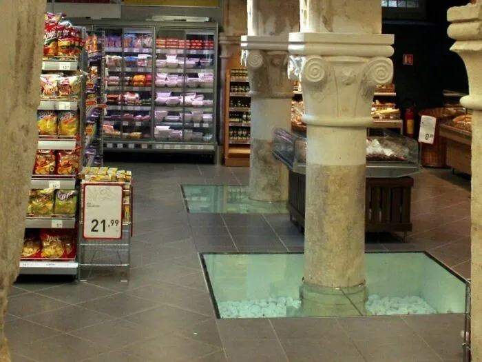 Supermarket inside ancient building with stone columns and glass floor, showcasing unique building conversions.