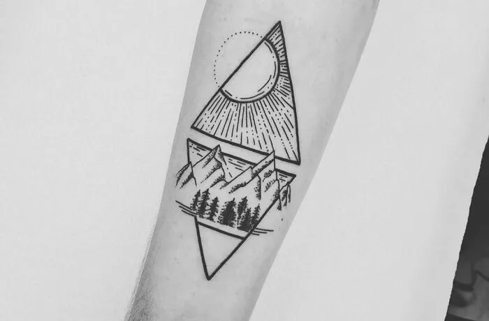 Geometric tattoo design featuring a triangle, sun, mountains, and trees on forearm.
