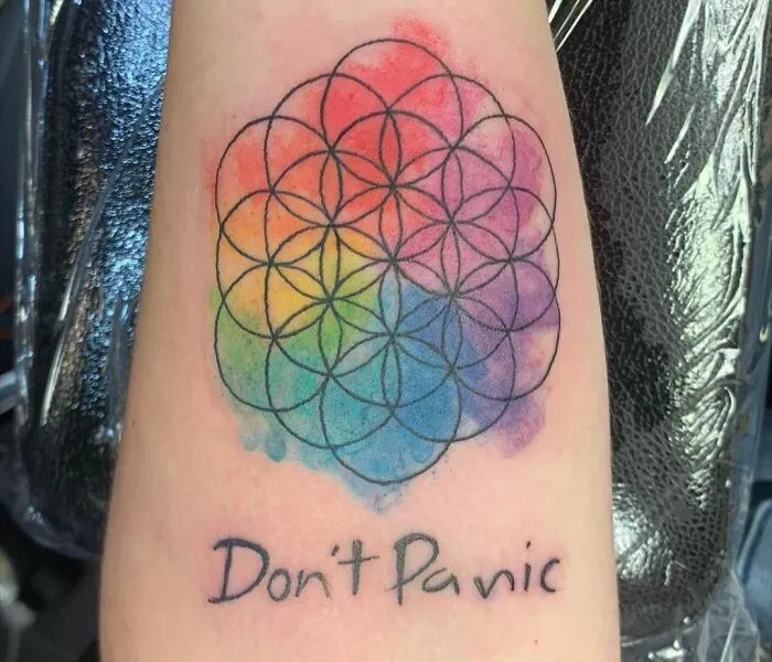 Geometric tattoo with colorful shapes and "Don't Panic" text, showcasing creativity.