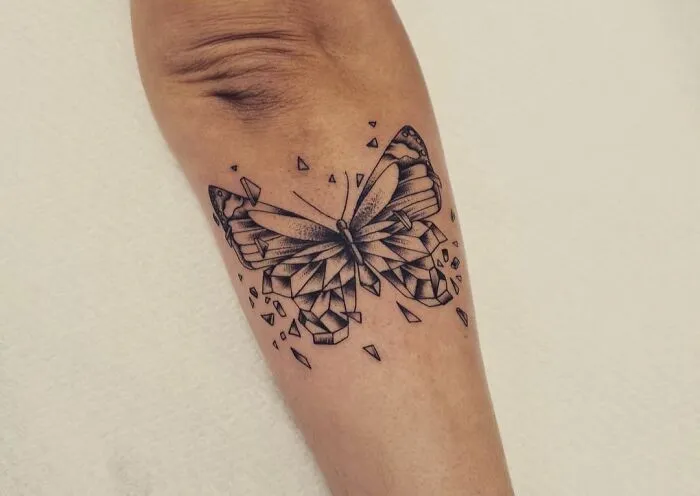 Geometric tattoo of a butterfly with fragmented shapes and creative patterns on a person's arm.